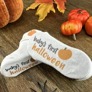 Baby's First Halloween socks with pumpkin graphic on wooden background and pumpkin, spider and fall leaf decorations