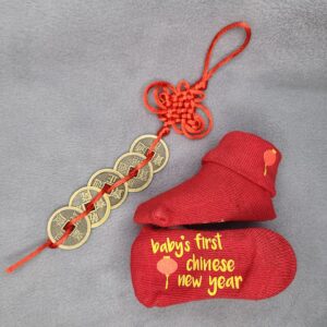 "Baby's First Chinese New Year" red sock with red lantern graphic and displayed with lucky Chinese knot and money coins, all on grey background