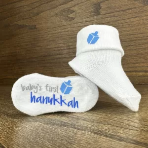 Baby's First Hanukkah socks with blue dreidel graphic on wooden background
