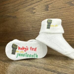 Baby's first Juneteenth sock with black fist graphic and broken gold chain with wood grain background